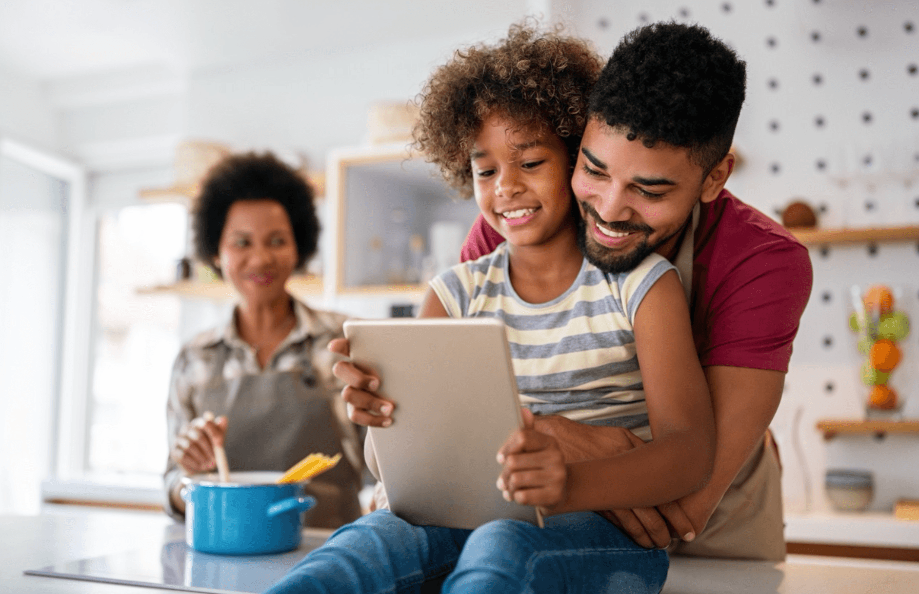 Smiling father looks over child’s shoulder as they use a tablet
