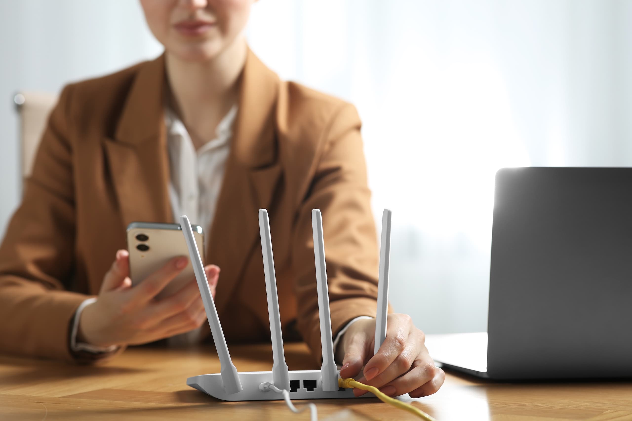Woman plugs ethernet cable into a modem router while holding a smart phone