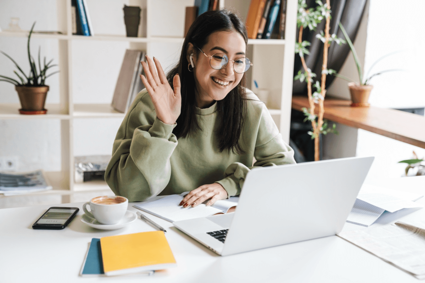 Happy woman waves to others on a video call on her laptop