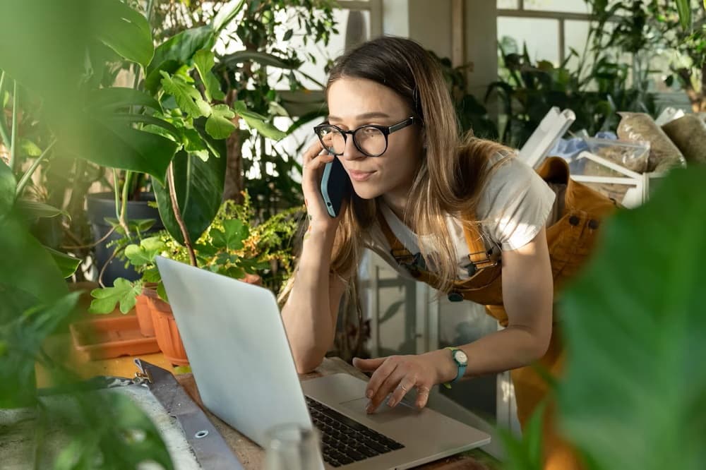 Young woman in glasses shopping online while talking on phone