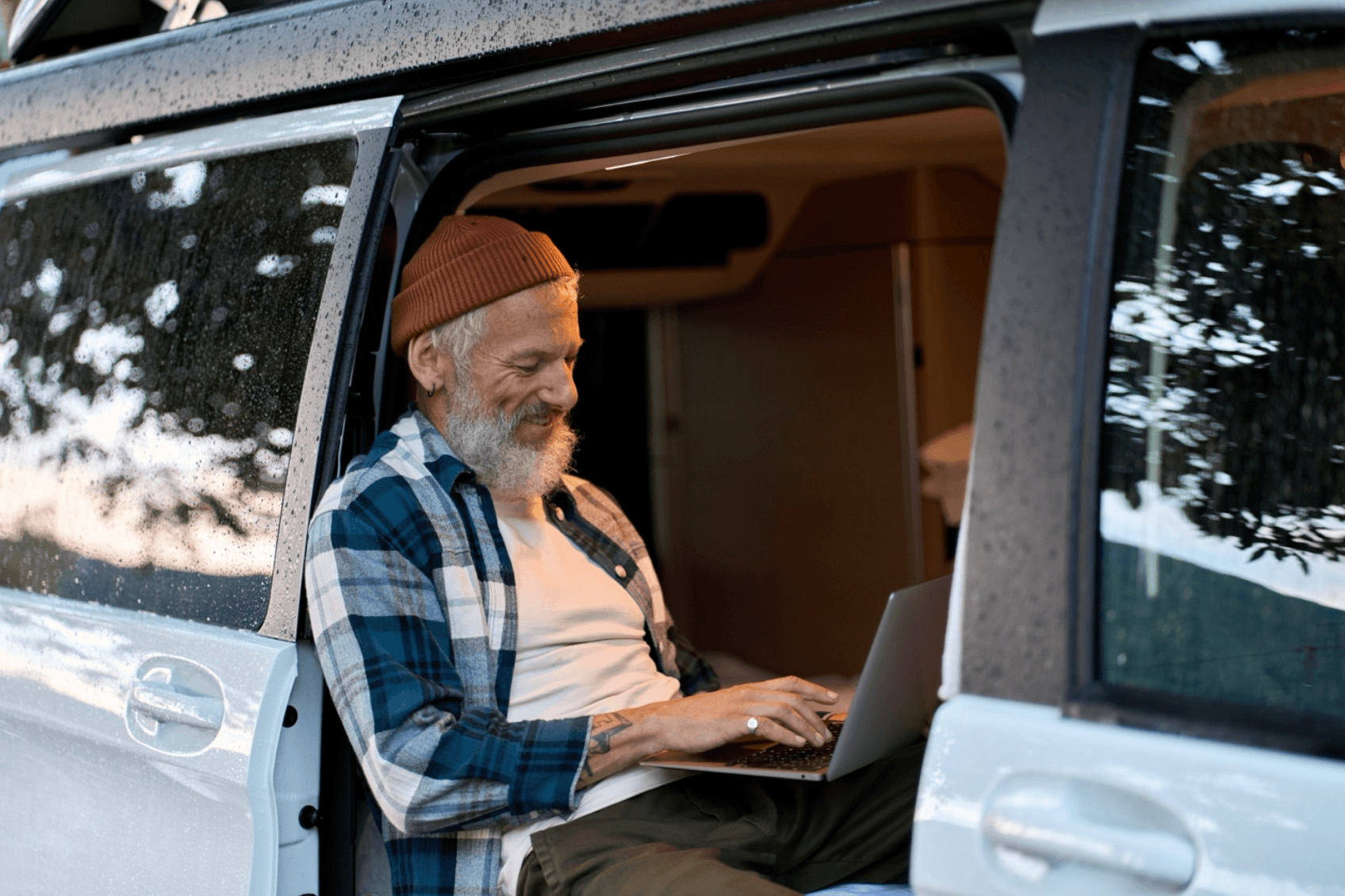 Man sits in his travel van while working on a laptop connected to a hotspot