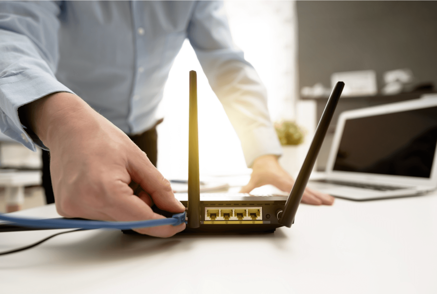 Man plugs in Ethernet cable to router with laptop in background