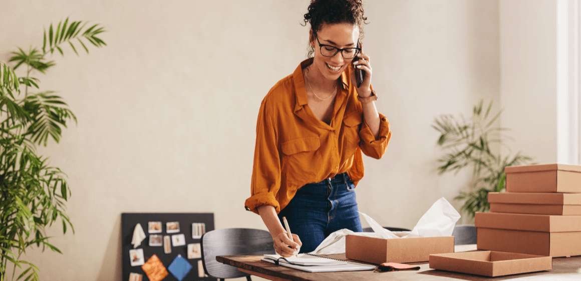 blog/A female entrepreneur working from her home office confirming an order while talking on the phone..png