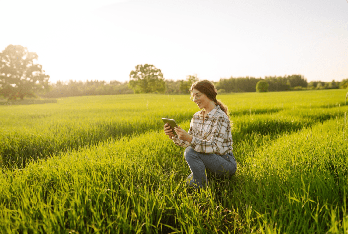 Farmer crouches in the field with a smart tablet in her hands