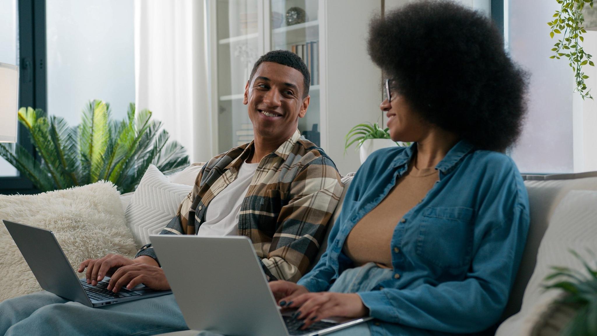 Smiling couple sits on the couch and works on their laptops