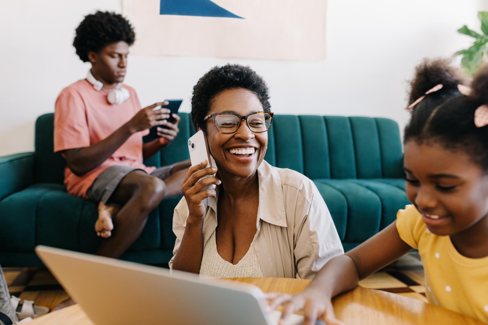 Woman smiles on the phone while daughter uses computer and son browses on tablet