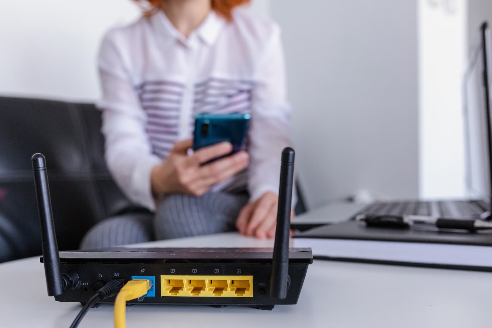 Wi-Fi router in foreground with woman connecting smartphone in the background