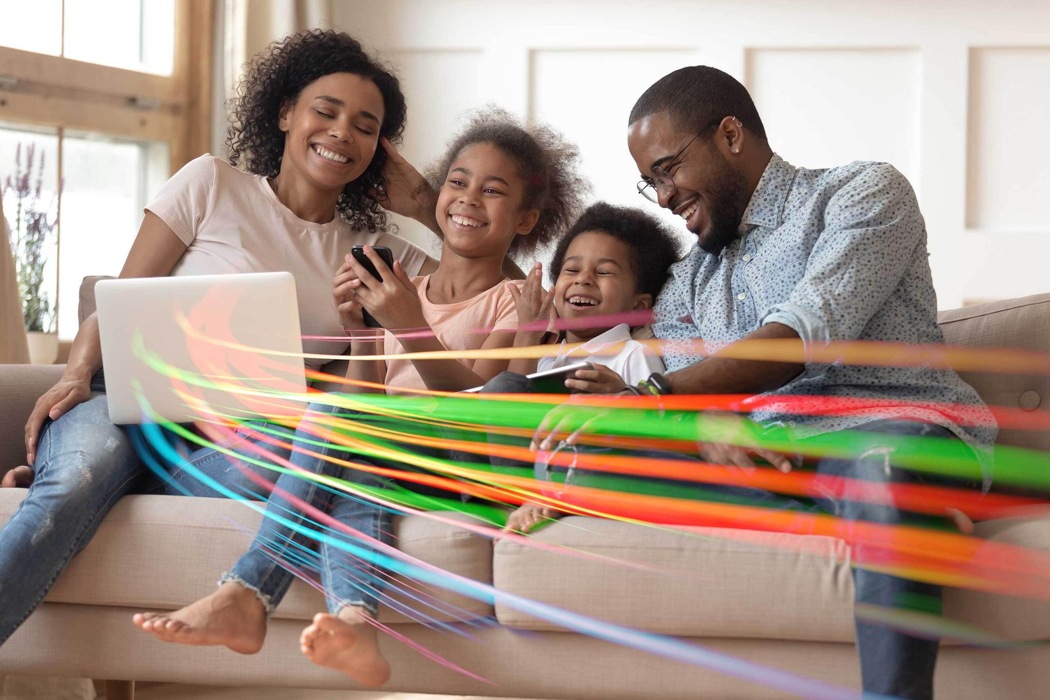 Family of four smiles and enjoys internet with ample bandwidth depicted as colored trails emanating from laptop.