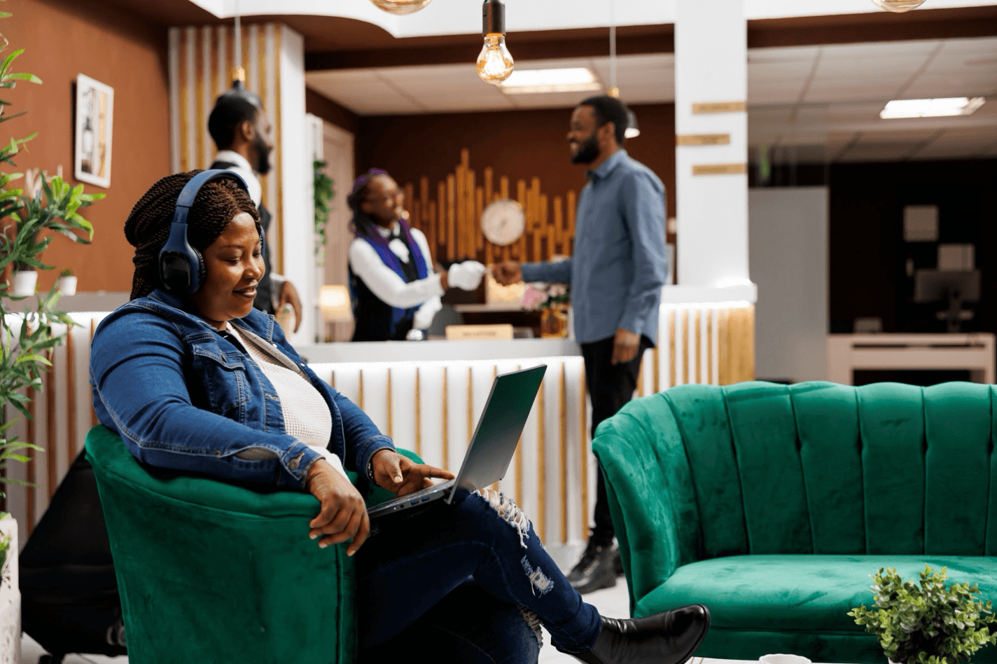 Happy woman sitting in hotel lobby with headphones and laptop