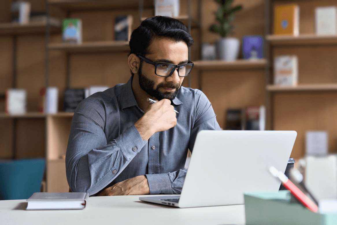Man with glasses looks at laptop with ponderous expression