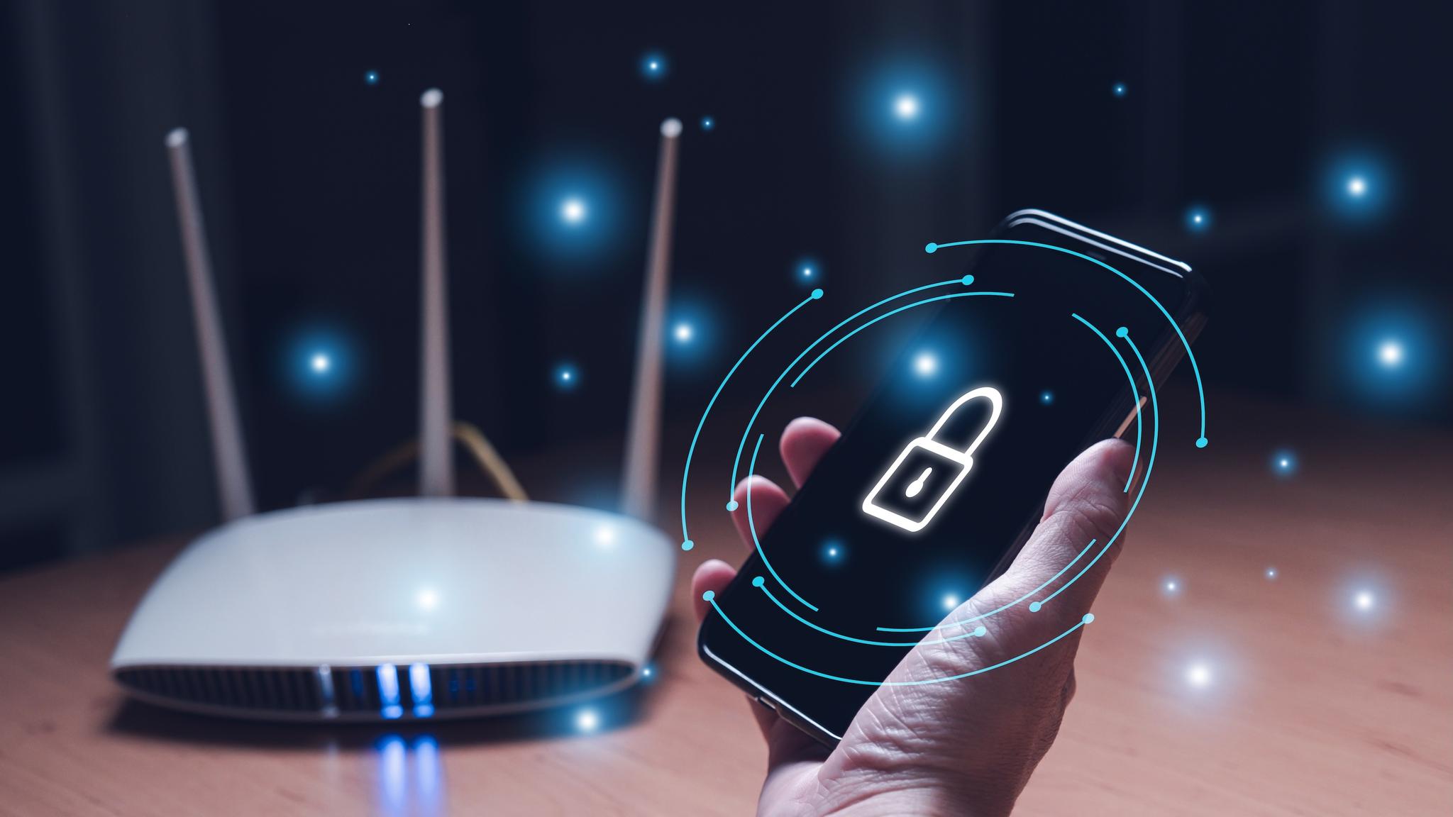 Hand holds a smart phone with a security icon with a router in the background