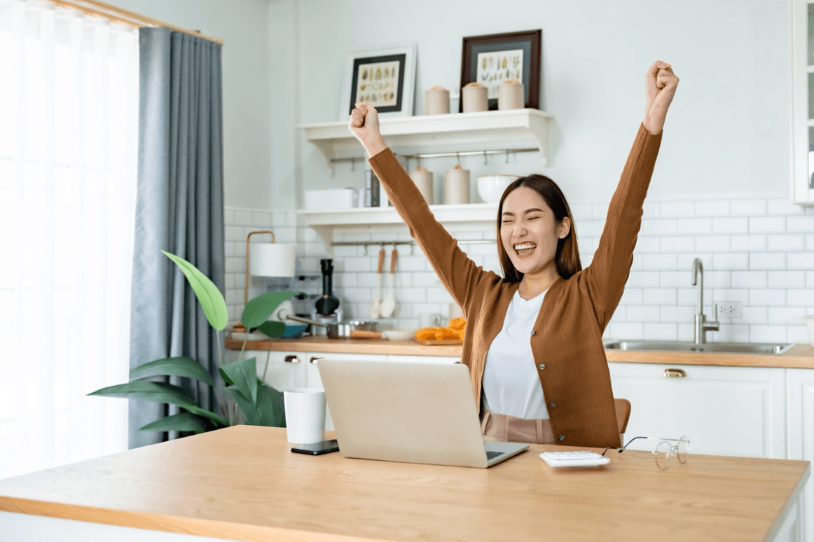 Happy woman puts hands up in celebration in front of laptop