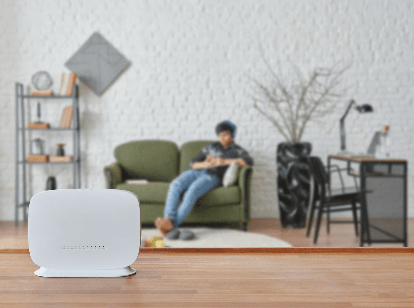 A network gateway in the foreground with a person sitting on a couch browsing on their phone in the background