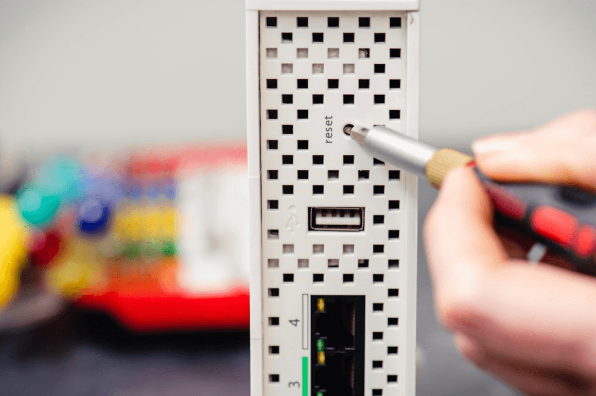 Person using small screwdriver to press factory reset button on router