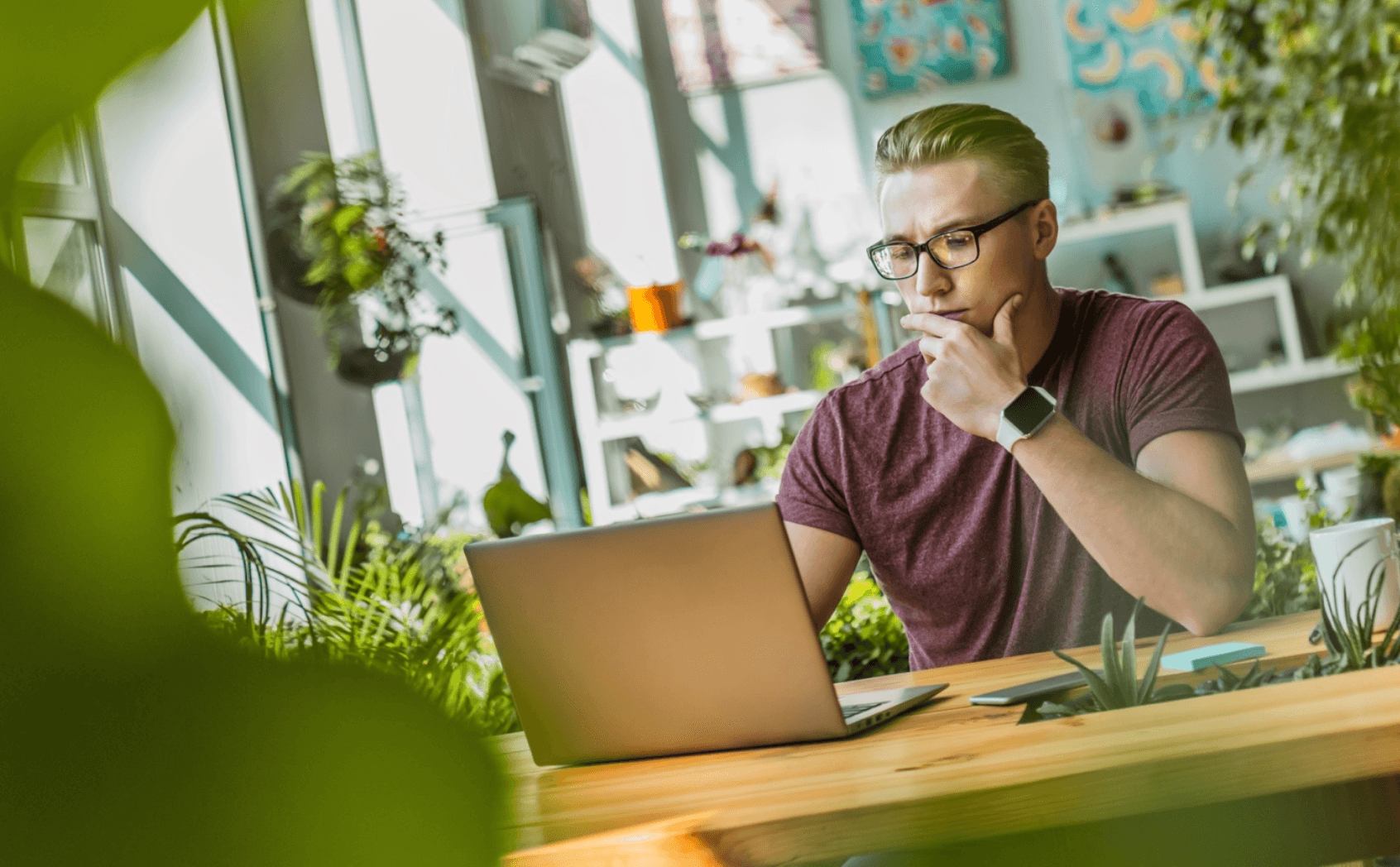 Man in public work space looks at computer with hand on chin