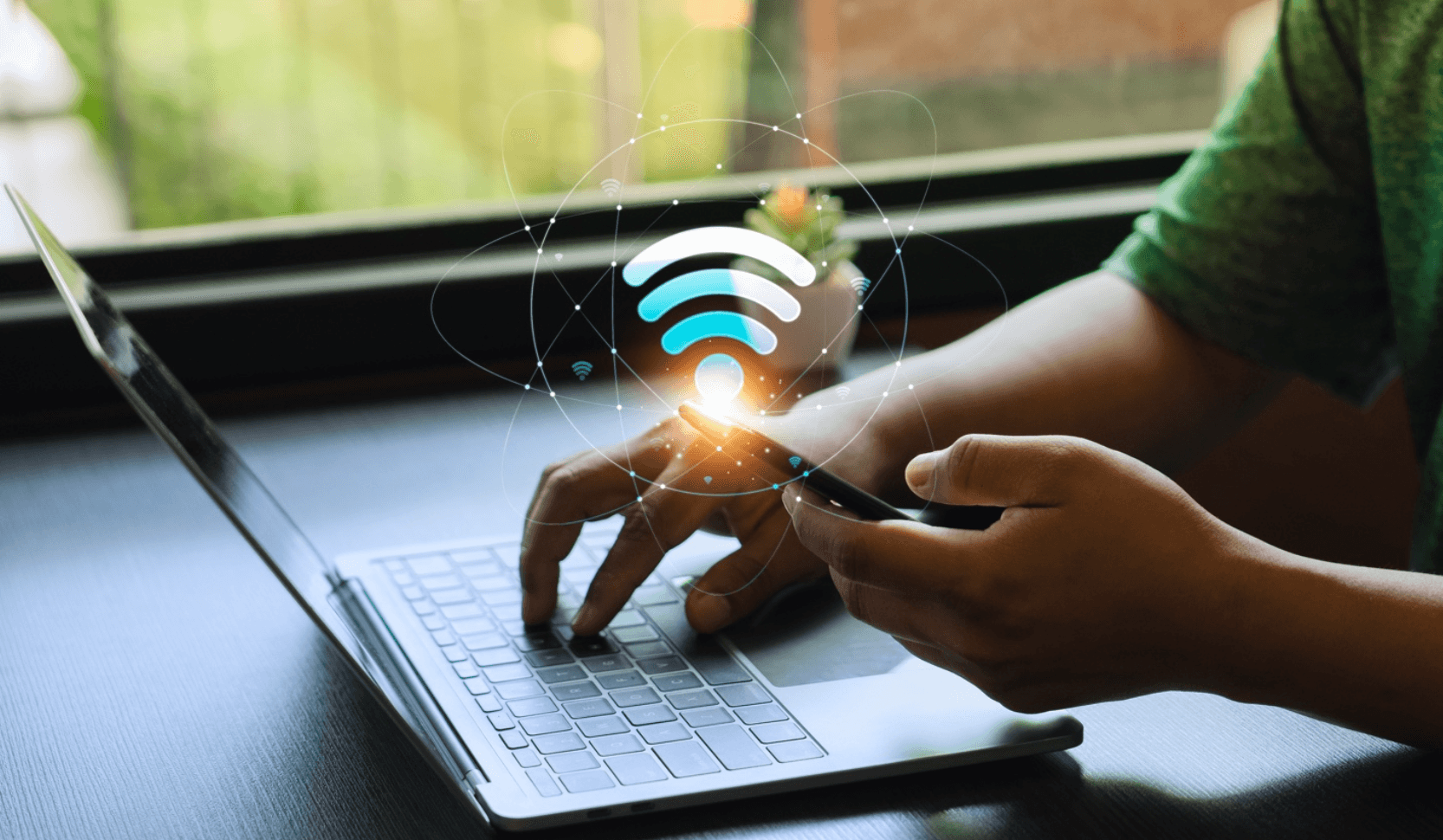 Person holds phone and types on laptop with hovering Wi-Fi signal