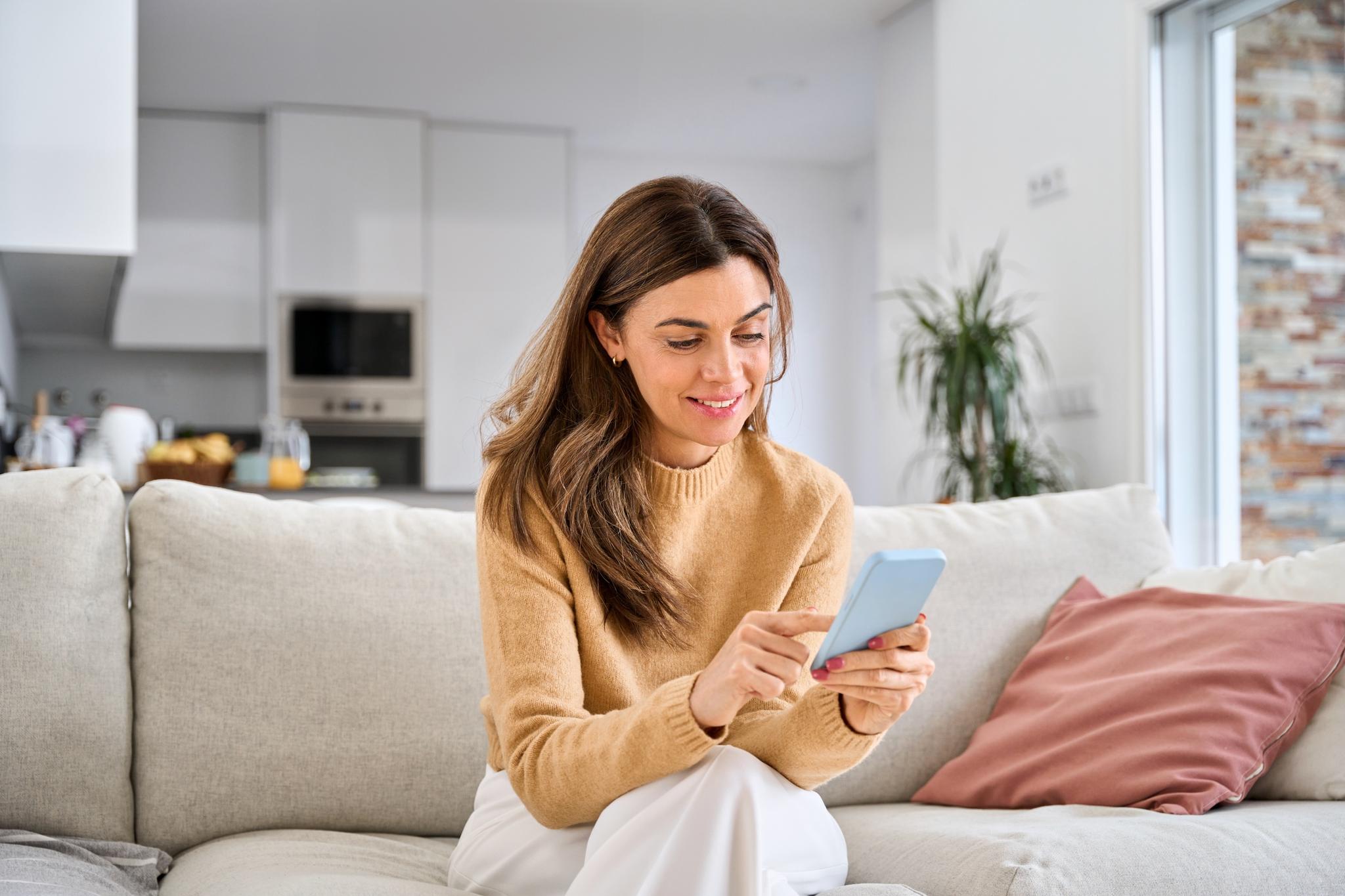 Woman sits on couch and connects her phone to Wi-Fi