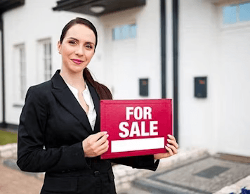 Realtor holds For Sale sign in front of home.