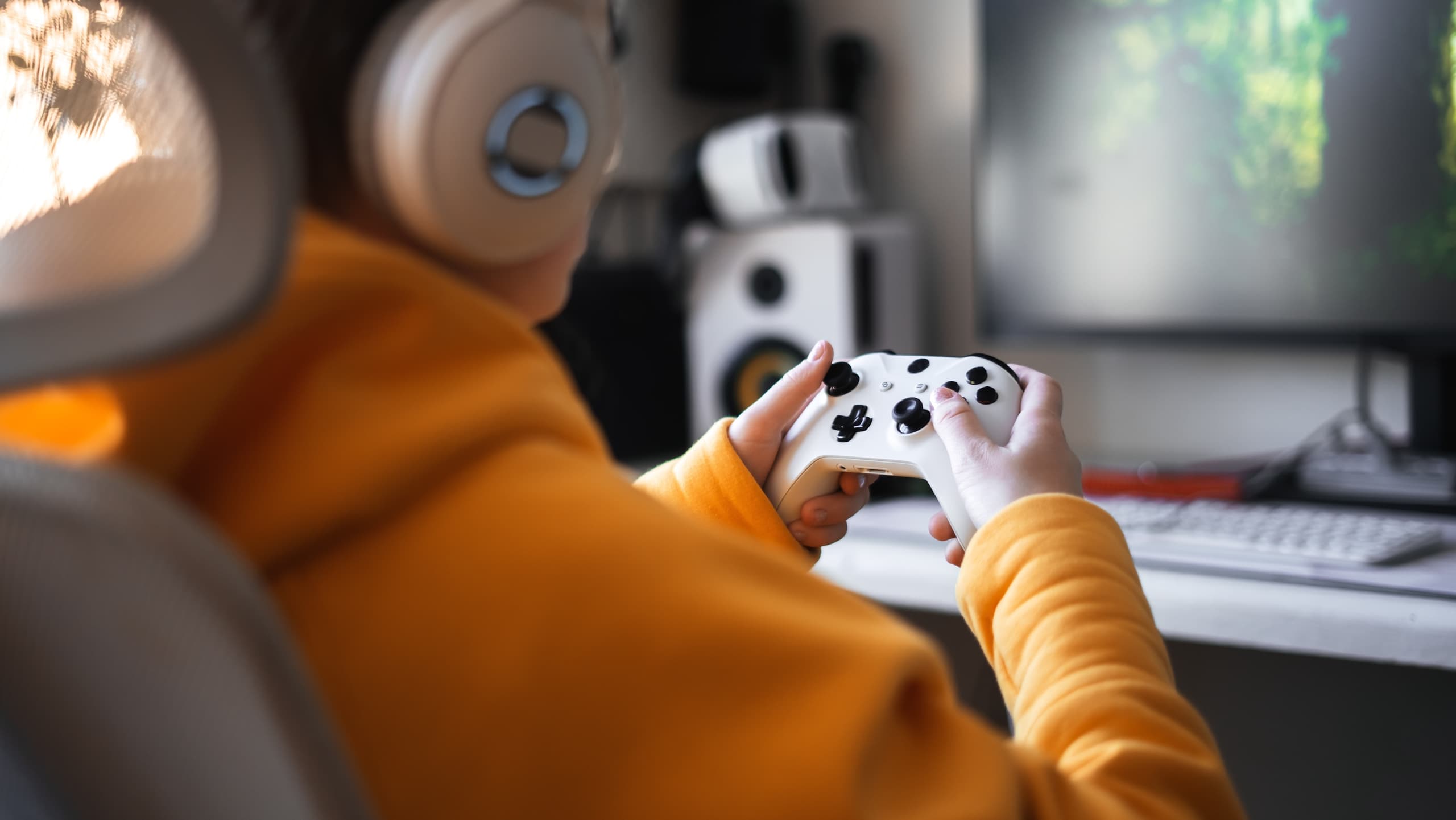 blog/A person holding a video game controller at a desk with a monitor, speakers, and gaming PC