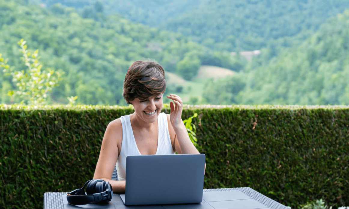 blog/Young woman smiling while looking at her laptop in a rural area.