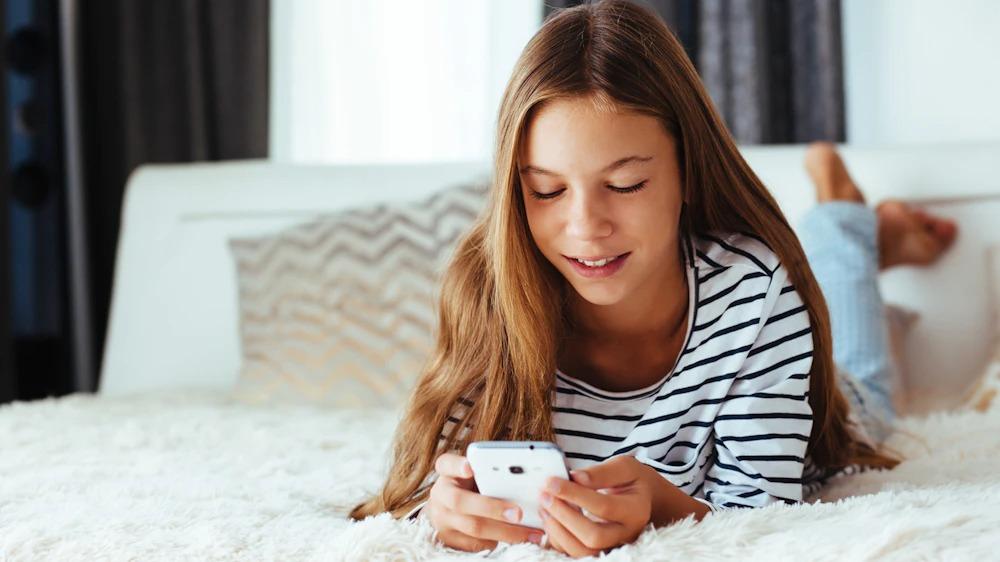 Teenage girl uses cell phone in bed