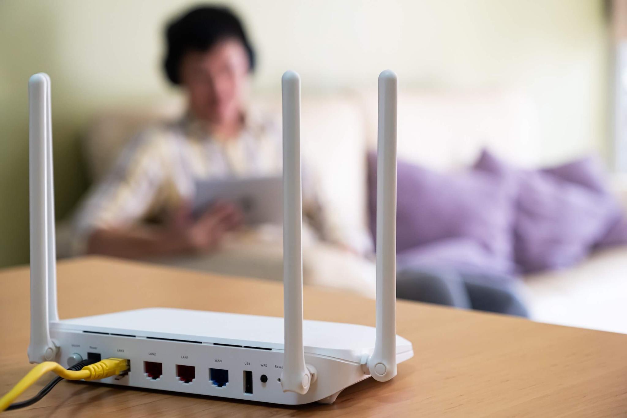 White Wi-Fi router in foreground with person on tablet in background