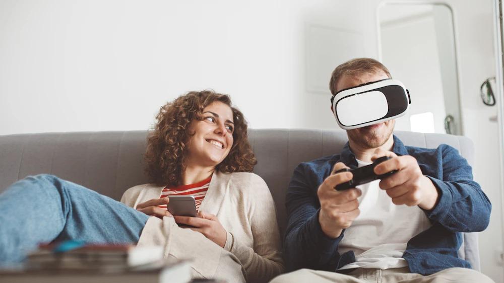 Man plays a game using a virtual reality headset while woman smiles and watches.