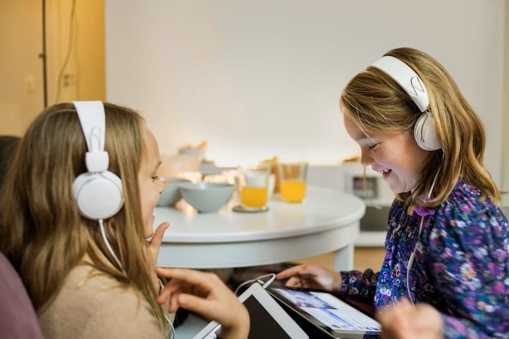 two young girls using tablets wearing headphones smiling