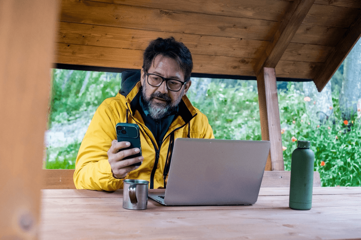 blog/Man in rural cabin checks phone with laptop in front of him.png