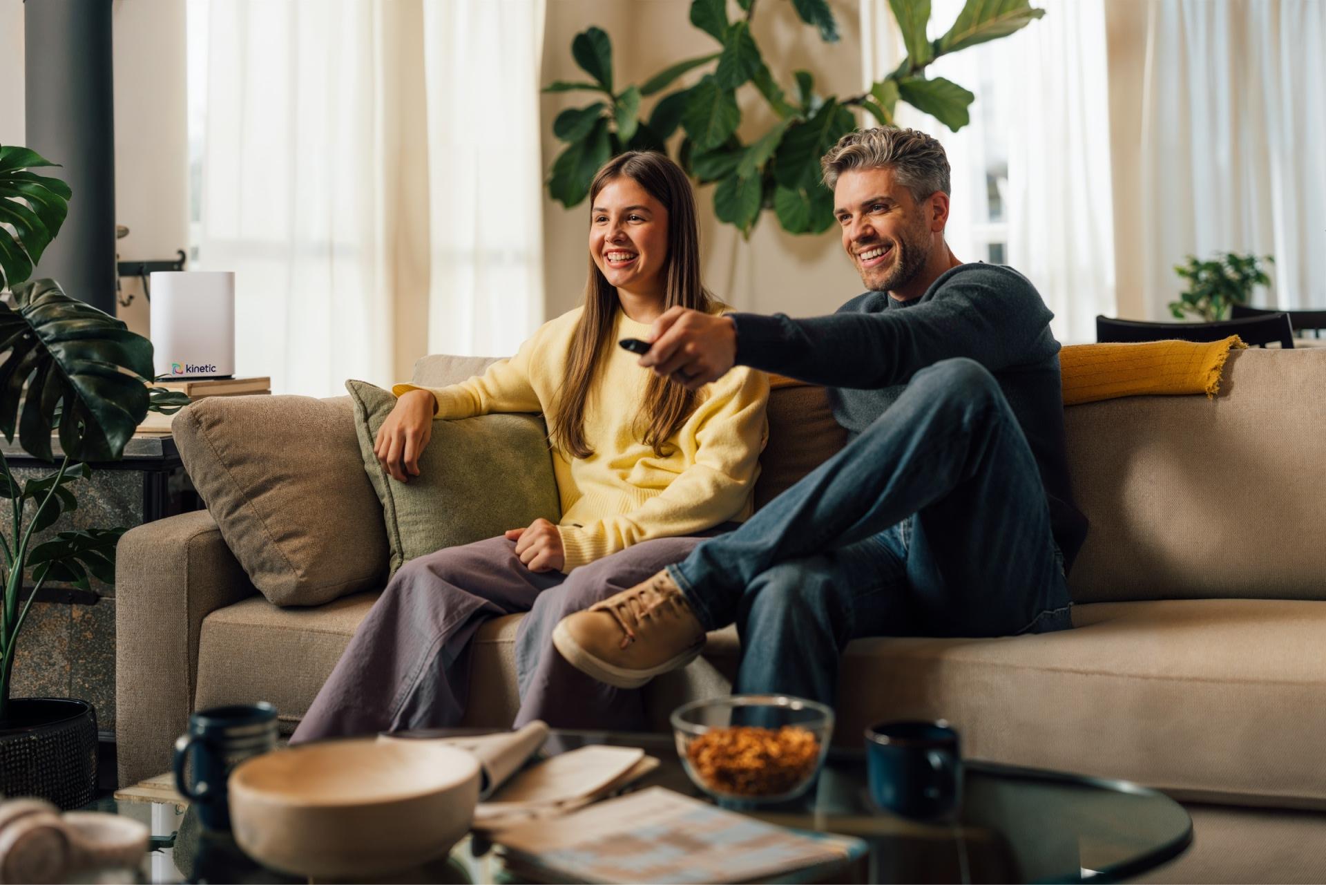 Father uses TV remote seated on couch next to his daughter as they watch television